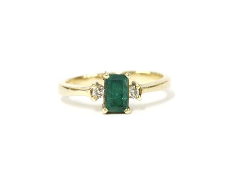 An emerald and diamond three stone ring, with an emerald cut emerald four claw set to the centre, stamped 18ct, tested and va