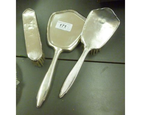 A three piece silver backed dressing table set, viz. two hair brushes and a mirror, each having engine turned decoration  Bir