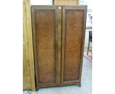 A 1930s walnut wardrobe, having two full height doors, enclosing a part fitted interior, raised on bracket feet  76''h  42''w