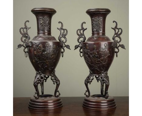 A pair of Japanese bronze vases with floral and foliate decoration, stylised bird handles on triform bases, 40cm high (2)Surf