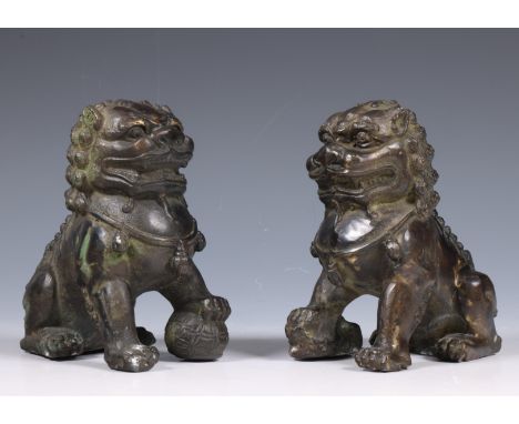 China, pair of bronze models of buddhist lions, 19th century, modelled in mirror image, one holding a brocade ball under its 