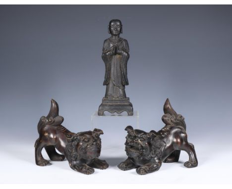China, pair of bronze Buddhist lions and a model of a monk, 20th century, the lions modelled in mirror image in crouching pos