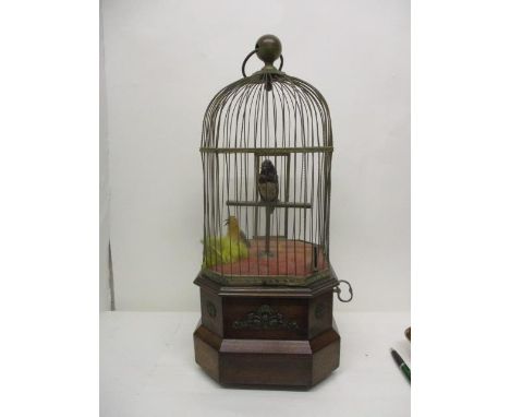 An early 20th century coin operated mahogany and brass, twin bird automaton with a carrying handle, a domed cage, one bird on