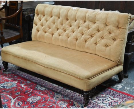 A Victorian button backed hall/banquette sofa, yellow-gold fabric, raised on turned mahogany front legs to castors (one brass