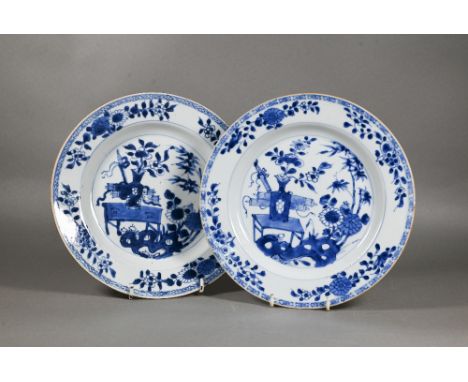 A pair of 18th century Chinese blue and white plates, painted with a vase of flowers on a table in a garden landscape setting