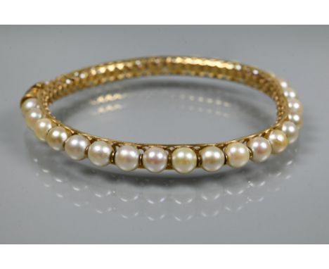 A yellow metal pearl-set bangle, the pierced open grill core set with thirty-one cultured pearls with spacers between, with s