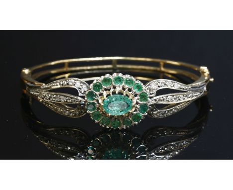 An emerald and diamond cluster hinged bangle, with an oval mixed cut emerald and circular mixed cut emerald centrepiece.  All