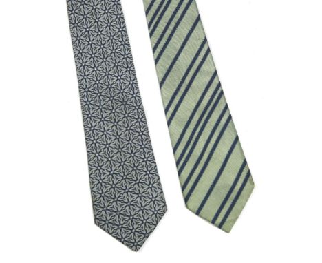 Two Hermès silk ties in boxes, to include a blue silk ground tie with a printed white and grey trefoil design, and a light gr