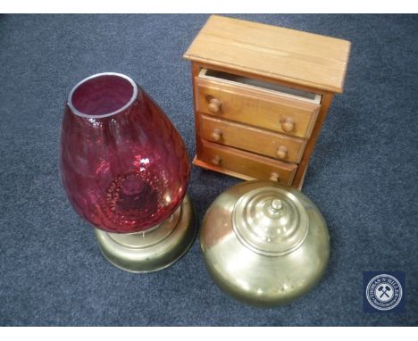 A miniature pine three-drawer chest together with a brass lidded urn and a brass oil lamp with cranberry glass shade 