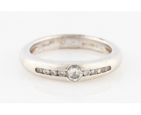 SOLD WITHOUT BUYERS PREMIUM AND VAT. A 9ct white gold diamond nine stone ring, channel set with a central round brilliant cut