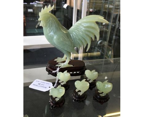 A carved jade cockerel figure together with five similar chicks, all having carved wooden stands.