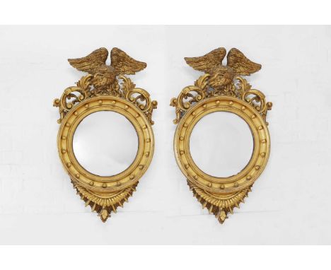 A pair of giltwood convex mirrors, 19th century and later, each mirror with an eagle surmount with foliate scrolls, the frame