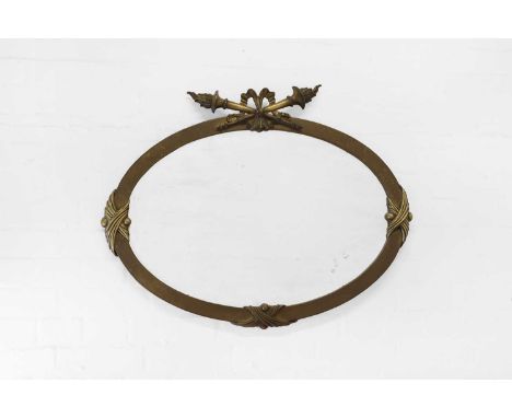 A brass oval mirror in the Louis XVI style, early 20th century, mounted by a pair of crossed torches and with a bevelled glas