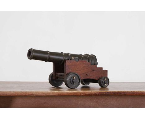 A patinated metal desk cannon, probably late 19th/early 20th century, with a turned barrel, raised on a stepped teak truckle 