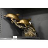 A 20th Century brass dolphin sculpture featuring two dolphins leaping over waves, raised upon a