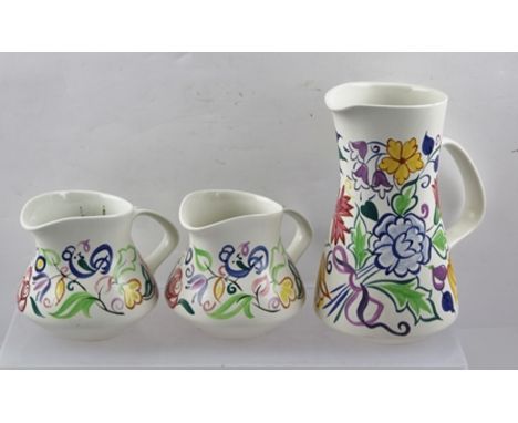 THREE POOLE POTTERY JUGS, hand painted stylized floral decoration, largest 19cm high 