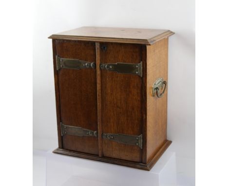 AN EDWARDIAN OAK SMOKER'S CABINET with Art Nouveau design shaped metal handles and hinges, opening to reveal drainers and rot