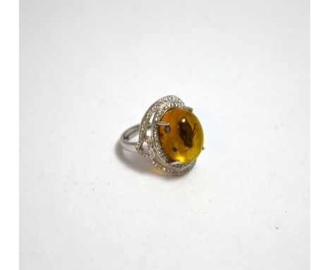 AN AMBER RING, with oval shape cabachon amber with fly inserted into the amber within a gemset mount, one stone deficient, ri
