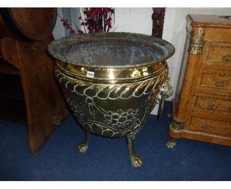 A LARGE BRASS EMBOSSED JARDINIERE/CAULDRON, with lions mask ring handles and tripod paw feet supports