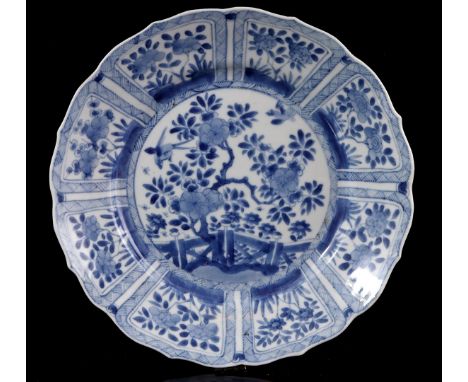 Porcelain dish with a contoured rim and a blue and white decoration of a garden with 8 areas in the rim with floral decoratio