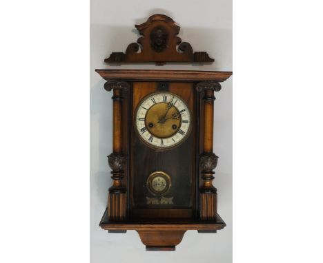 A small late 19th Century walnut Vienna wall clock the shaped fret cut pediment centred on a female mask, the circular dial w