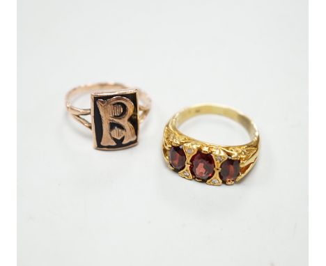 A yellow metal and three stone garnet set ring, with diamond chip spacers and a 9ct and black enamel set initial ring, gross 