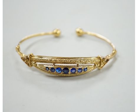 A 750 yellow metal and graduated seven stone sapphire?, paste and doublet set open work bangle, gross weight 12.1 grams.