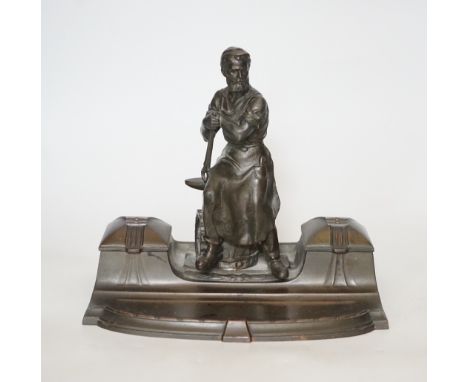 A WMF style spelter ‘Industry’ inkstand, figure with tools and an anvil, hinged ink wells either side, one glass ink bottle p