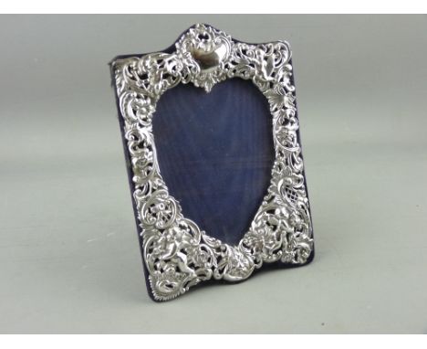 A SILVER EASEL PORTRAIT FRAME, the heart shaped reveal surrounded by cherubic floral and latticed scrolling, London 1894, max