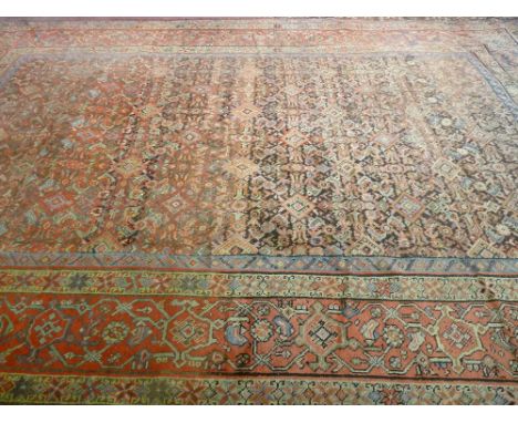 A LARGE RED GROUND PATTERNED WOOLLEN CARPET with multiple border, 453 x 340 cms (quite worn with some repairs)