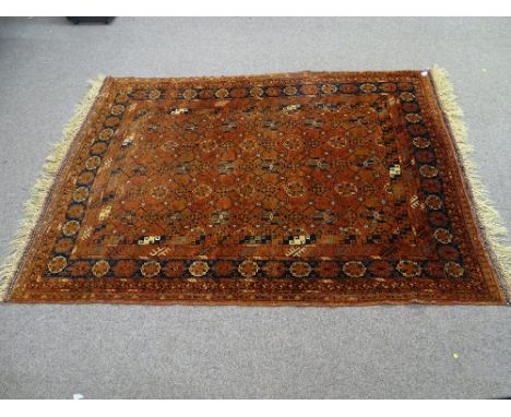 AN EASTERN STYLE TUFTED WOOL CARPET, rust ground with repeating central pattern and multi-bordered edge with tasselled ends, 