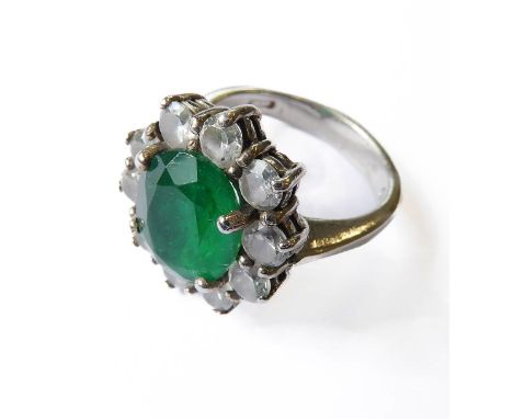 A silver ring (marked 925), centrally set with a green emerald-like oval stone surrounded by ten further, smaller white stone