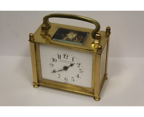 Squat brass carriage clock, with swing handle above the visible escapement, the white dial with Roman numerals and retailers 