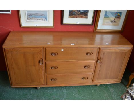 A light elm Ercol sideboard, three long drawers flanked by cupboards.