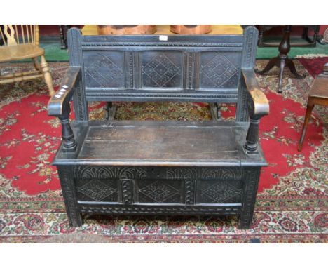 A carved oak hall seat, carved panel back, open arms, hinged seat, three carved panels to front, stile feet, circa 1810.