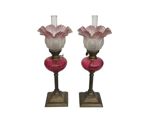 Pair of small brass oil lamps with ruby glass reservoirs and tinted pink frosted shades, 44cm.