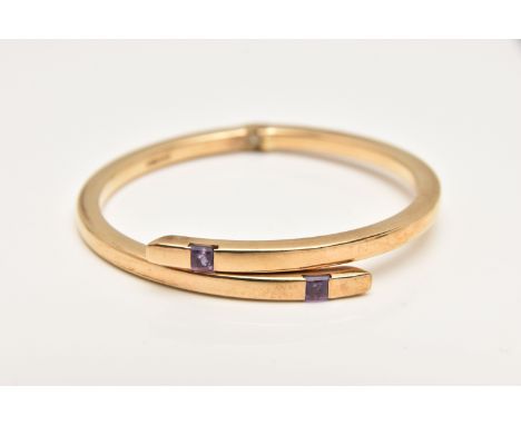 A 9CT GOLD AMETHYST BANGLE, the crossover bangle with sprung hinge, set to each terminal with a square shape amethyst, hallma