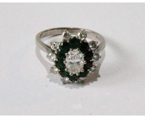 Dress ring with oval diamond brilliant surrounded by ten emeralds and ten smaller brilliants, in 18ct white gold, 1977. Condi