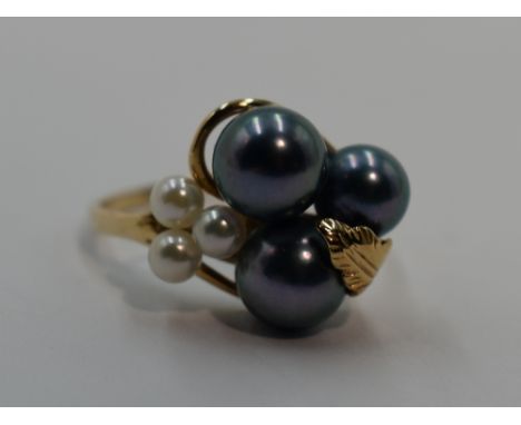 A lady's dress ring having black and white cultured pearls in a yellow metal stylised mount on a yellow metal loop, no marks,