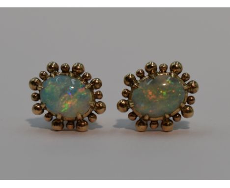 A pair of stud earrings having oval light opal cabouchons in yellow metal claw set ball mounts, stamped 18K, both opals throw