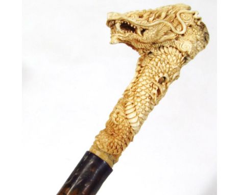 A Chinese walking stick, with carved dragon antler top, white metal collar and tapering stem, heavily carved, the dragon with