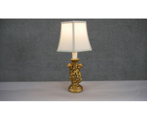 A gilded plaster cherub design table lamp with cream hexagonal shade. H.47 W.26cm 