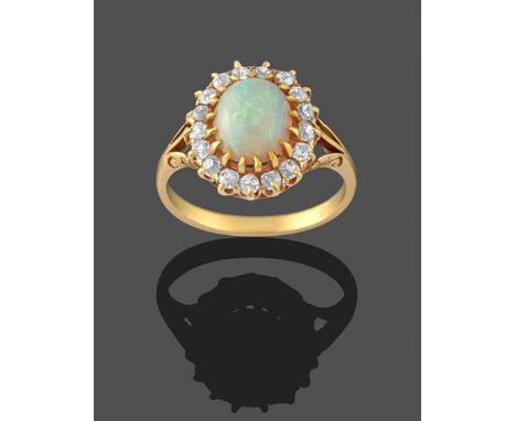 An Opal and Diamond Cluster Ring, the oval opal cabochon within a border of old cut diamonds in yellow claw settings, to a tr