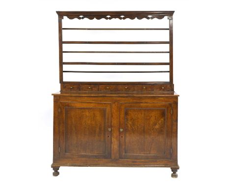 An oak dresser, 18th century, the open plate rack back over a bank of spice drawers, three frieze drawers and with cupboards 