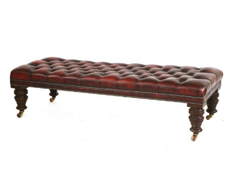 A large button upholstered leather footstool, the rectangular top on ring turned tapering legs and castors