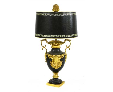 A gilt and black metal table lamp, of urn shape with a leather covered toleware shade, mounted on a carved and painted column