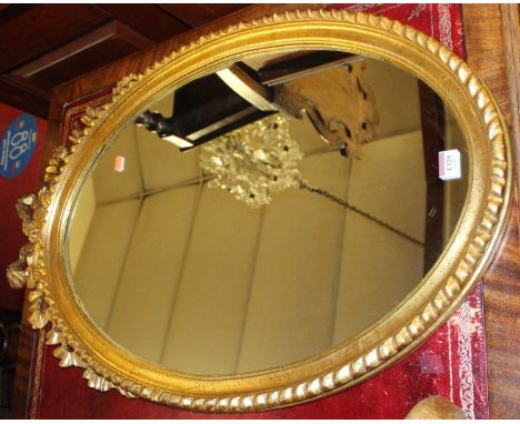A contemporary gilt wood oval wall mirror, having ribbon floral surmount and gadrooned outer edge, 88 x 54.5cm