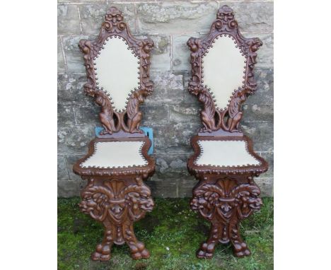A pair of Continental carved hall chairs, with upholstered panel to the back and seat, decorated with mythical creatures