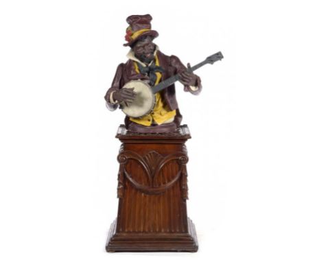 A COLD PAINTED TERRACOTTA HALF FIGURE OF A BANJO PLAYER POSSIBLY GOLDSCHEIDER 76cm h and a carved, mahogany stained wood pede