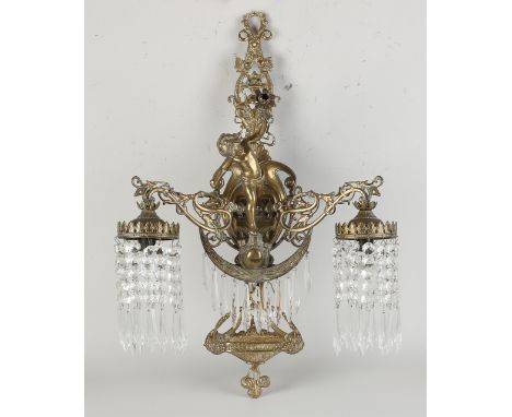 Two-light brass wall lamp with putti and prism glass.&nbsp;20th century.&nbsp;Dimensions: 63 cm.&nbsp;In good condition.